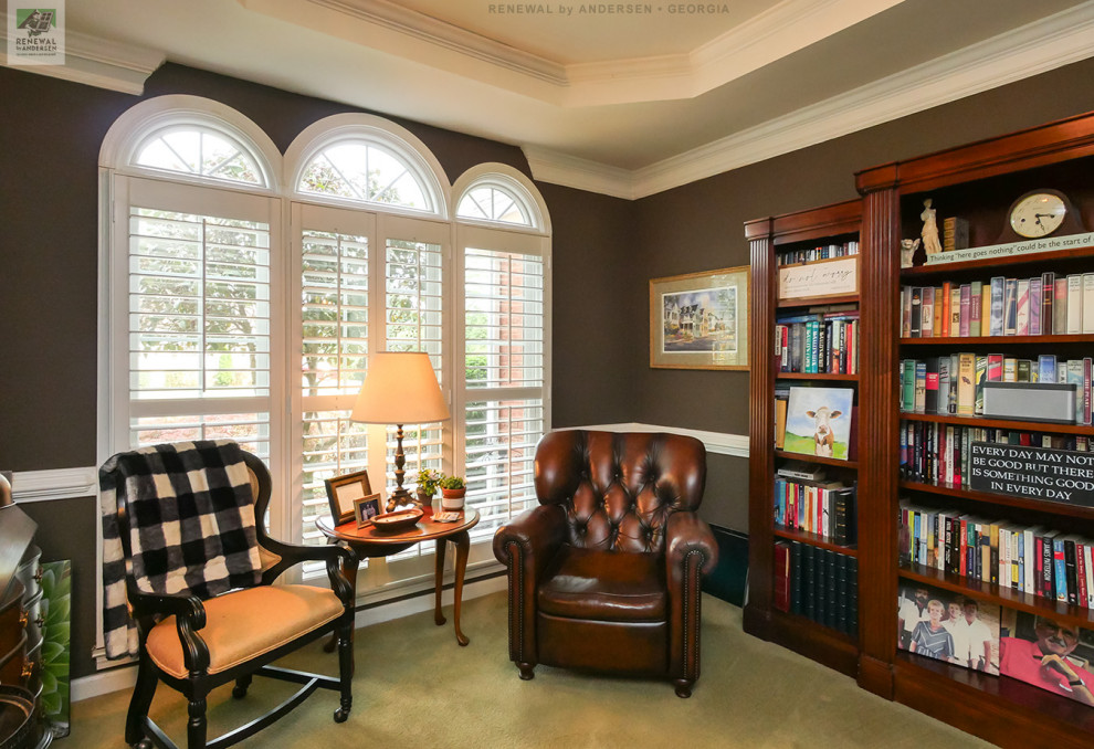 Bild på ett mellanstort hemmabibliotek, med bruna väggar, heltäckningsmatta, ett fristående skrivbord och grönt golv