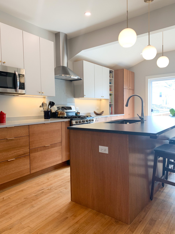 Photo of a large midcentury single-wall eat-in kitchen in Chicago with an undermount sink, white cabinets, quartz benchtops, white splashback, engineered quartz splashback, stainless steel appliances, medium hardwood floors, with island, brown floor and white benchtop.