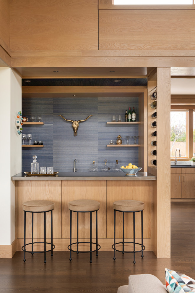 This is an example of a mid-sized contemporary galley wet bar in Minneapolis with an undermount sink, flat-panel cabinets, light wood cabinets, zinc benchtops, blue splashback, medium hardwood floors and brown floor.