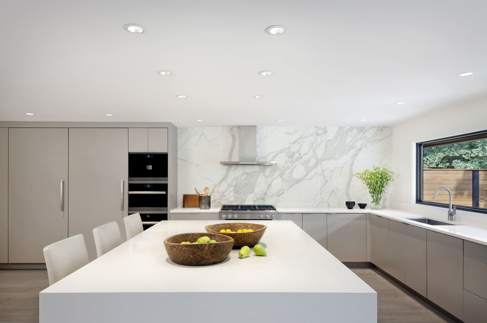 Inspiration for a contemporary l-shaped kitchen in Seattle with an undermount sink, flat-panel cabinets, grey cabinets, white splashback, stone slab splashback, light hardwood floors, with island, grey floor and white benchtop.