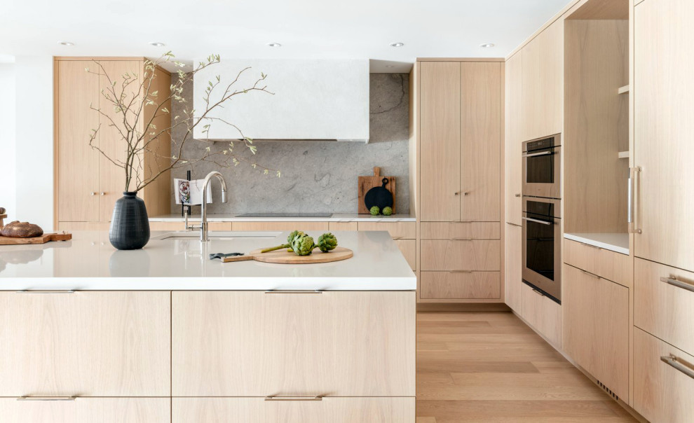 Inspiration for a mid-sized modern l-shaped eat-in kitchen in Vancouver with a double-bowl sink, flat-panel cabinets, light wood cabinets, solid surface benchtops, grey splashback, limestone splashback, panelled appliances, light hardwood floors, with island, beige floor and white benchtop.