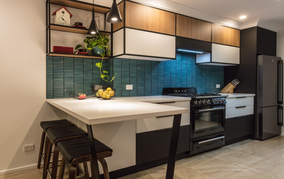 Design ideas for a mid-sized midcentury galley eat-in kitchen in Sydney with a drop-in sink, flat-panel cabinets, white cabinets, solid surface benchtops, green splashback, mosaic tile splashback, black appliances, ceramic floors, no island, beige floor and white benchtop.