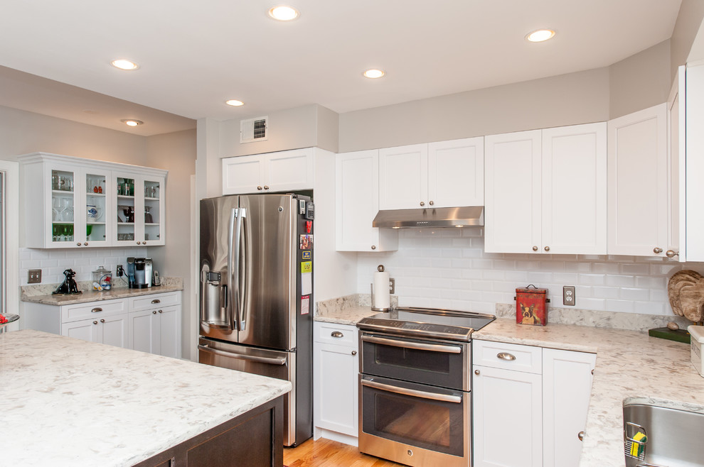 Inspiration for a mid-sized transitional l-shaped eat-in kitchen in DC Metro with an undermount sink, shaker cabinets, white cabinets, granite benchtops, white splashback, subway tile splashback, stainless steel appliances, light hardwood floors and with island.