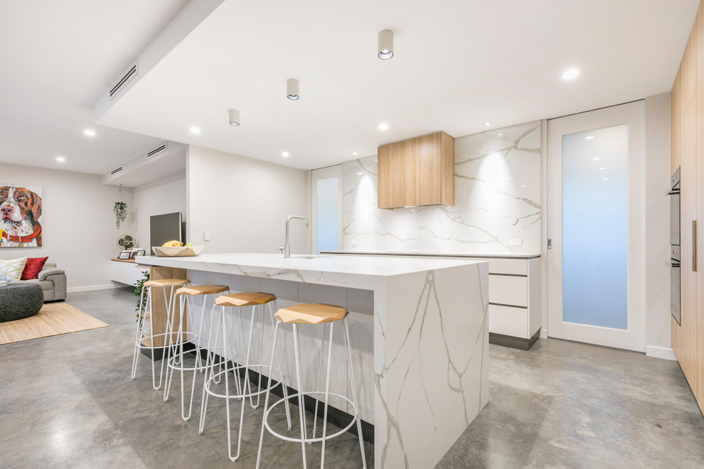 Inspiration for a large modern galley kitchen pantry in Canberra - Queanbeyan with an undermount sink, flat-panel cabinets, white cabinets, quartz benchtops, white splashback, stone slab splashback, black appliances, concrete floors, with island, grey floor and white benchtop.