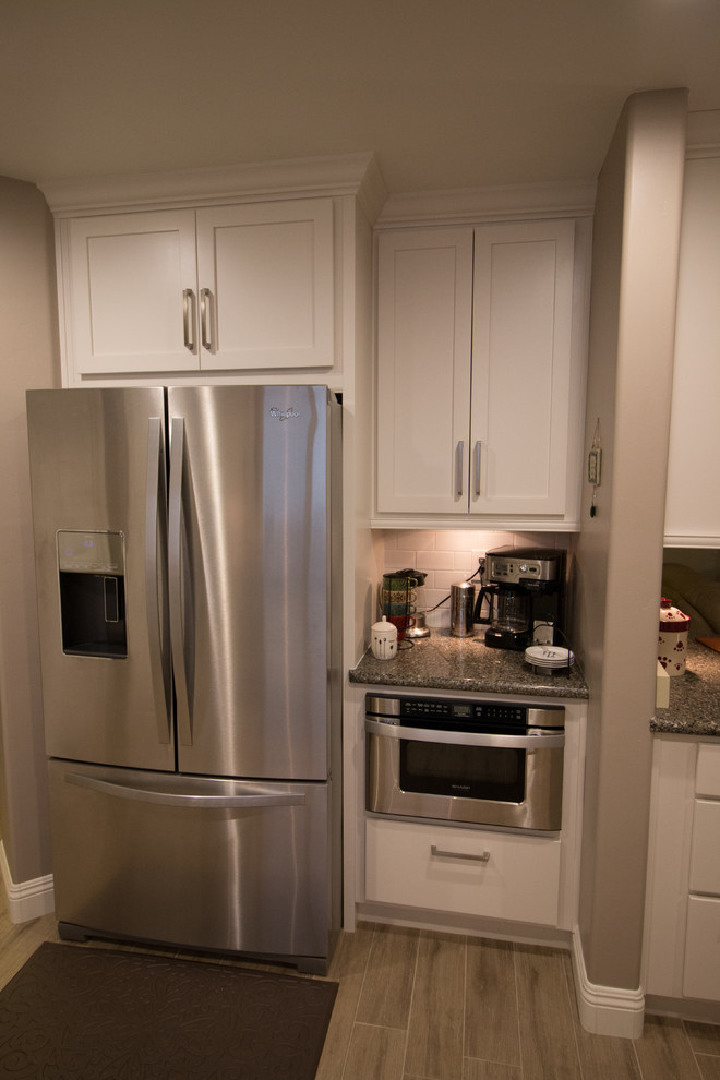 Example of a mid-sized transitional galley porcelain tile open concept kitchen design with a farmhouse sink, shaker cabinets, white cabinets, quartz countertops, white backsplash, subway tile backsplash and stainless steel appliances