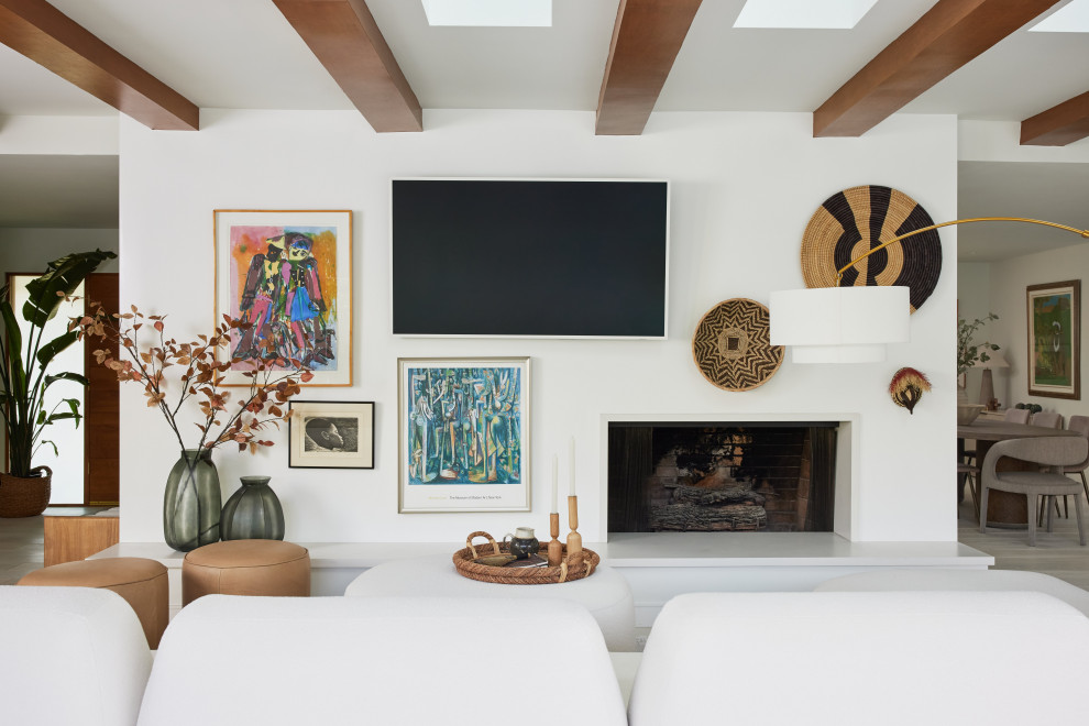 This is an example of a large midcentury open plan games room in Los Angeles with white walls, light hardwood flooring, a standard fireplace, a wall mounted tv, beige floors and exposed beams.