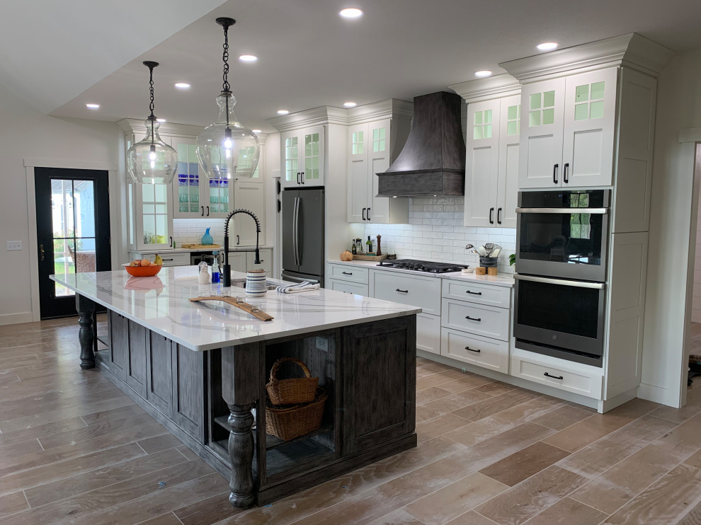 Inspiration for a large rustic l-shaped brown floor open concept kitchen remodel with an undermount sink, recessed-panel cabinets, white cabinets, quartz countertops, white backsplash, stainless steel appliances, an island and white countertops