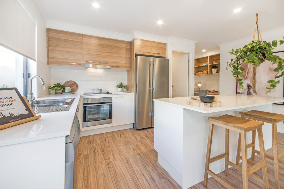 This is an example of a large contemporary eat-in kitchen in Sunshine Coast with a drop-in sink, flat-panel cabinets, light wood cabinets, white splashback, subway tile splashback, stainless steel appliances, light hardwood floors and with island.
