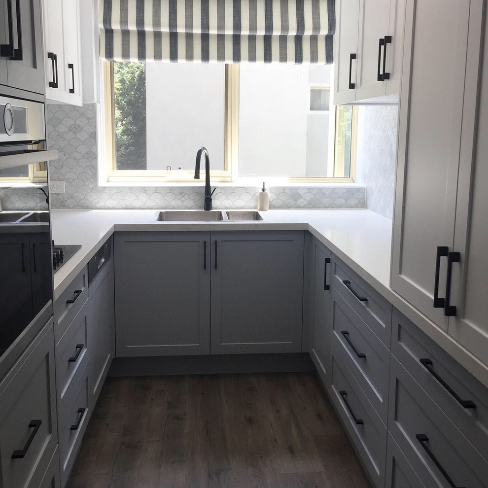 This is an example of a small contemporary u-shaped separate kitchen in Melbourne with a drop-in sink, shaker cabinets, grey cabinets, quartz benchtops, grey splashback, marble splashback, black appliances, laminate floors, no island, grey floor and white benchtop.