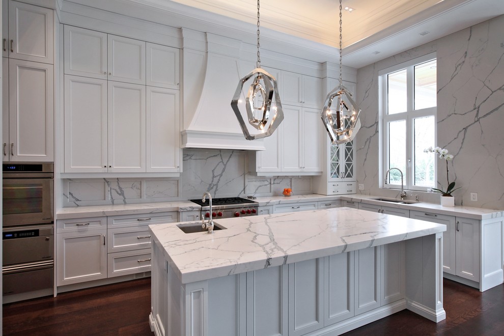 This is an example of a large transitional u-shaped open plan kitchen in Toronto with a double-bowl sink, shaker cabinets, white cabinets, marble benchtops, white splashback, stone slab splashback, stainless steel appliances, dark hardwood floors, with island and brown floor.