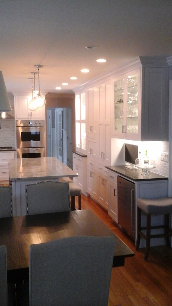 Example of a mid-sized transitional l-shaped light wood floor eat-in kitchen design in Newark with a double-bowl sink, shaker cabinets, white cabinets, solid surface countertops, multicolored backsplash, stone tile backsplash, stainless steel appliances and an island