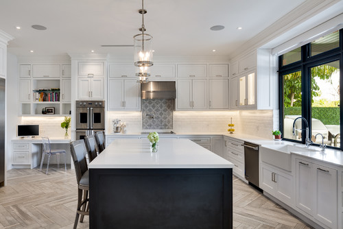 Bright kitchen with white Shaker cabinet doors (recessed panels) and chrome pulls, contrasting charcoal island, herringbone floor, black-framed window, subway backsplash, and pendant lights