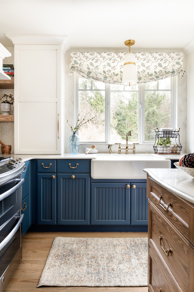Inspiration for a mid-sized u-shaped kitchen in Seattle with a farmhouse sink, recessed-panel cabinets, blue cabinets, quartzite benchtops, white splashback, limestone splashback, stainless steel appliances, medium hardwood floors, with island, brown floor and blue benchtop.