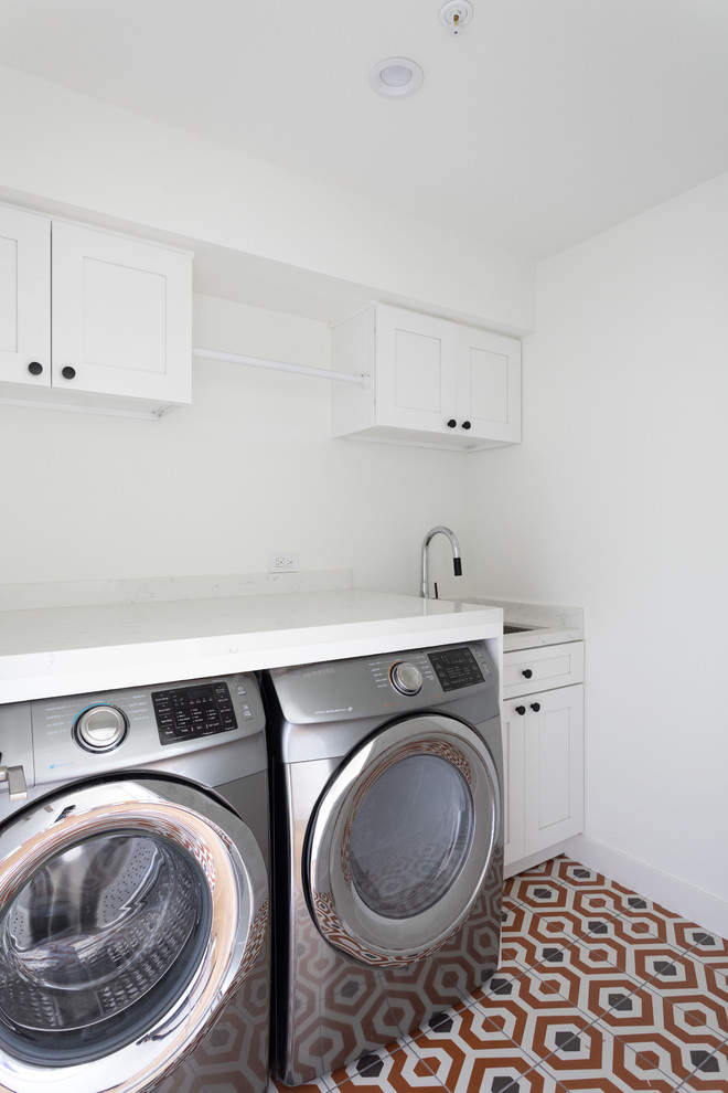 Photo of a transitional single-wall dedicated laundry room in Los Angeles with an undermount sink, recessed-panel cabinets, white cabinets, quartzite benchtops, white walls, ceramic floors, a side-by-side washer and dryer, orange floor and white benchtop.