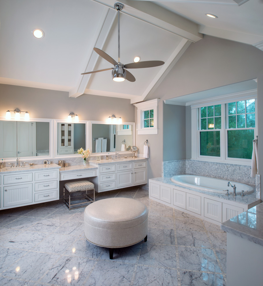 This is an example of a large traditional master bathroom in Houston with white cabinets, a drop-in tub, an undermount sink, beaded inset cabinets, marble benchtops, white tile, stone tile, grey walls, marble floors, a corner shower, a two-piece toilet, grey floor, a hinged shower door and white benchtops.