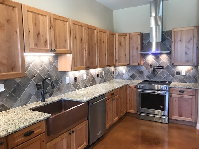 Mid-sized country u-shaped open plan kitchen in Austin with a farmhouse sink, recessed-panel cabinets, medium wood cabinets, granite benchtops, grey splashback, ceramic splashback, stainless steel appliances, concrete floors, a peninsula and brown floor.