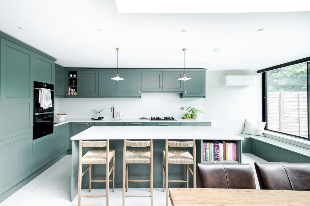 This is an example of a medium sized modern l-shaped open plan kitchen in Surrey with an integrated sink, shaker cabinets, green cabinets, quartz worktops, white splashback, limestone splashback, integrated appliances, concrete flooring, a breakfast bar, grey floors and white worktops.