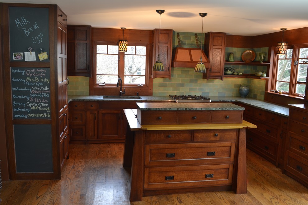 Inspiration for a mid-sized arts and crafts u-shaped eat-in kitchen in Philadelphia with a double-bowl sink, flat-panel cabinets, dark wood cabinets, soapstone benchtops, green splashback, ceramic splashback, panelled appliances, medium hardwood floors and with island.