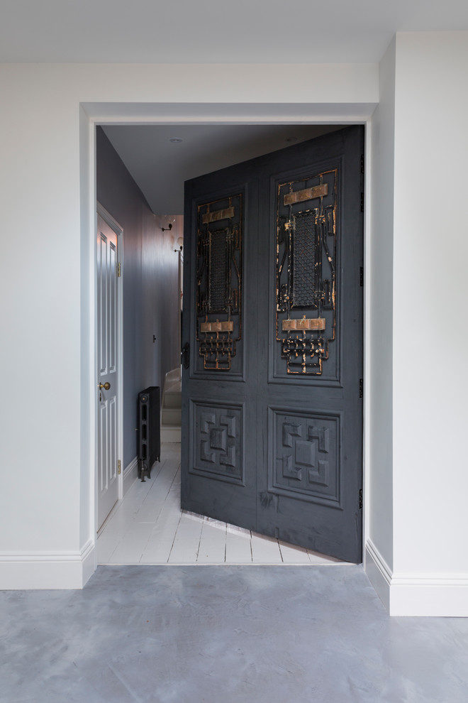Photo of a large eclectic front door in London with white walls, concrete floors, a single front door, a black front door and grey floor.