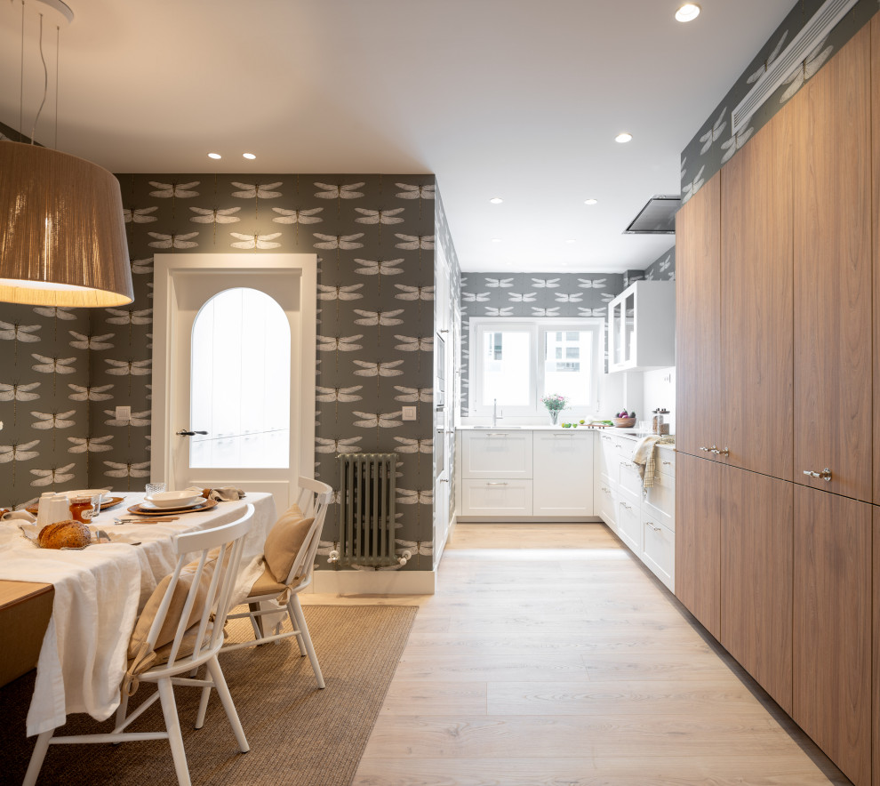 Large transitional l-shaped eat-in kitchen in Bilbao with an undermount sink, flat-panel cabinets, white cabinets, quartz benchtops, white splashback, engineered quartz splashback, stainless steel appliances, laminate floors, no island, brown floor and white benchtop.