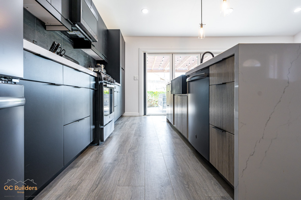 Inspiration for a large modern galley open plan kitchen in Orange County with a belfast sink, flat-panel cabinets, black cabinets, laminate countertops, black splashback, metro tiled splashback, black appliances, plywood flooring, an island, beige floors, white worktops and a vaulted ceiling.