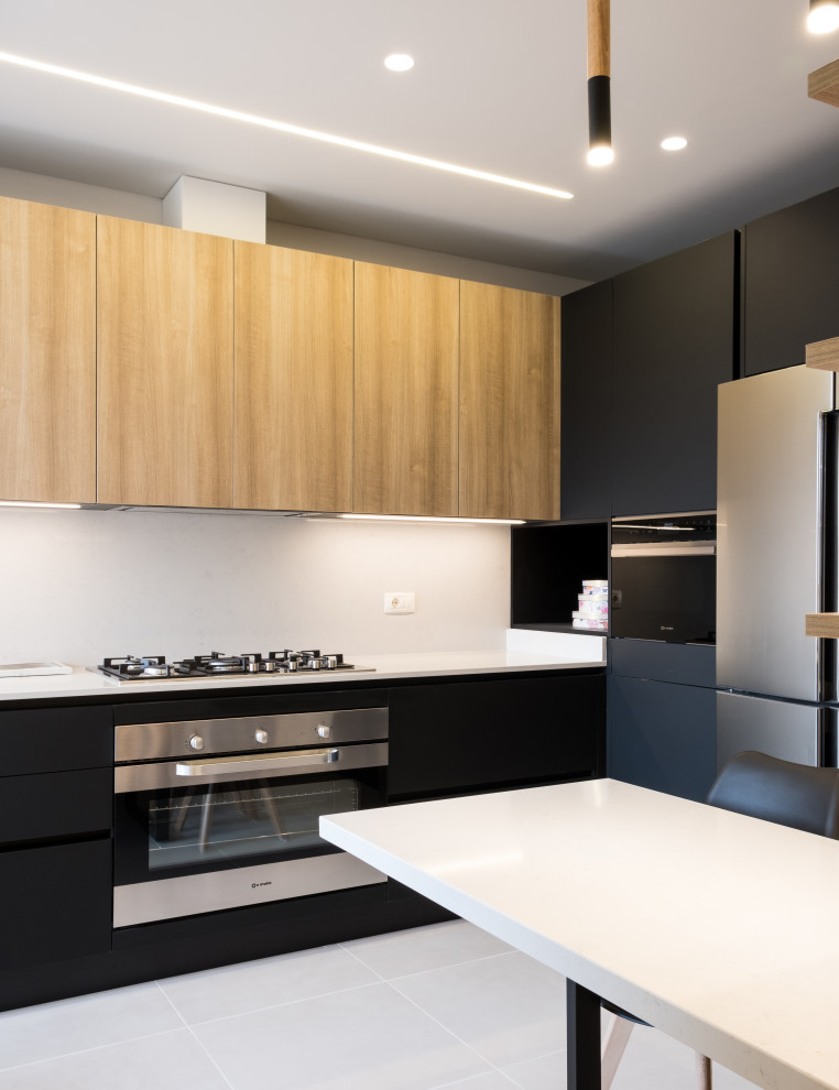 This is an example of a medium sized modern l-shaped kitchen/diner in London with an integrated sink, black cabinets, engineered stone countertops, white splashback, engineered quartz splashback, stainless steel appliances, limestone flooring, no island, white worktops, a drop ceiling and feature lighting.