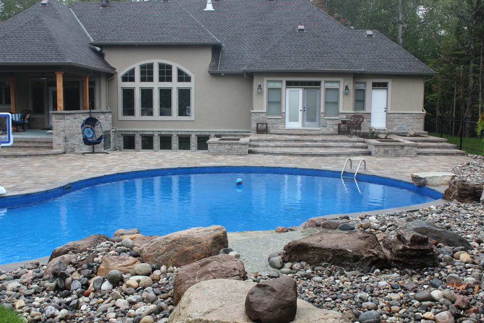 Photo of a large contemporary backyard kidney-shaped natural pool in Ottawa with a water feature and stamped concrete.