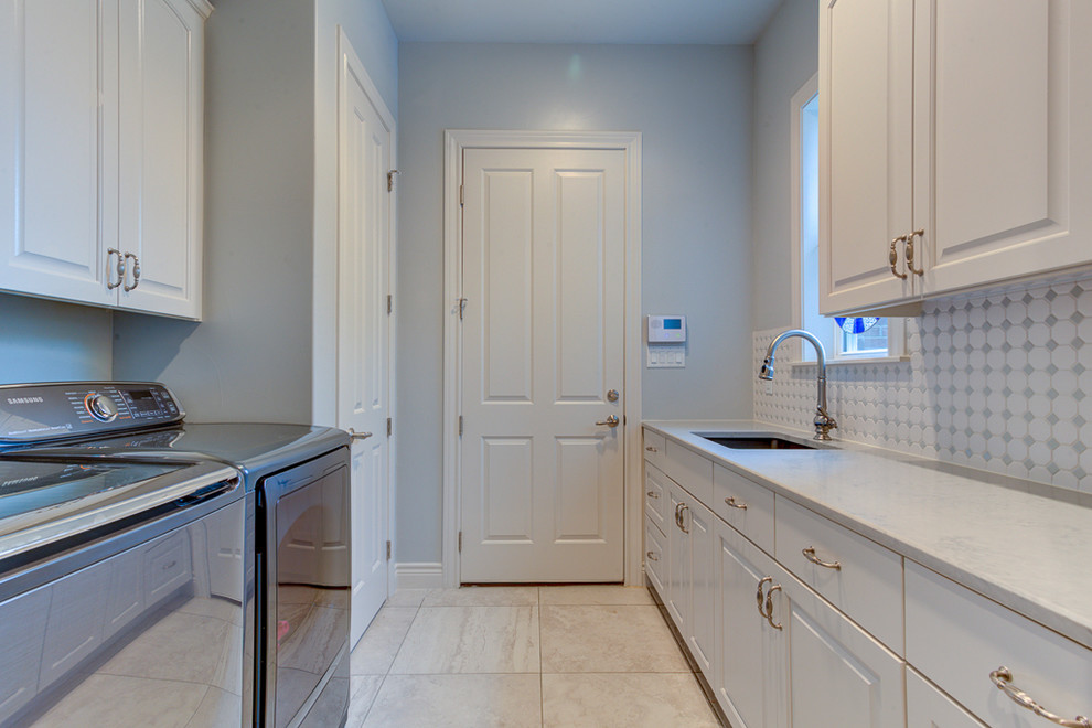 Mid-sized traditional galley dedicated laundry room in Austin with an undermount sink, raised-panel cabinets, white cabinets, quartz benchtops, blue walls, porcelain floors, a side-by-side washer and dryer, grey floor and white benchtop.