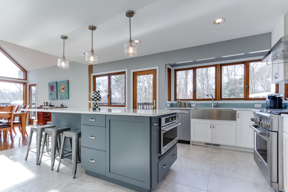 This is an example of a transitional u-shaped eat-in kitchen in DC Metro with a farmhouse sink, shaker cabinets, white cabinets, quartz benchtops, blue splashback, subway tile splashback and stainless steel appliances.