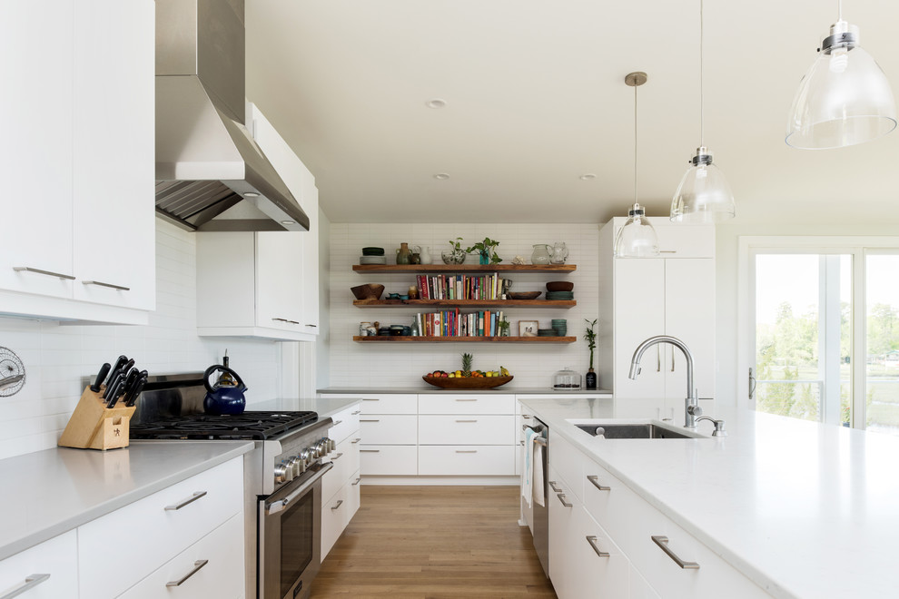 Inspiration for a mid-sized eclectic l-shaped eat-in kitchen in Other with an undermount sink, flat-panel cabinets, white cabinets, quartzite benchtops, white splashback, ceramic splashback, stainless steel appliances, light hardwood floors, with island and white benchtop.