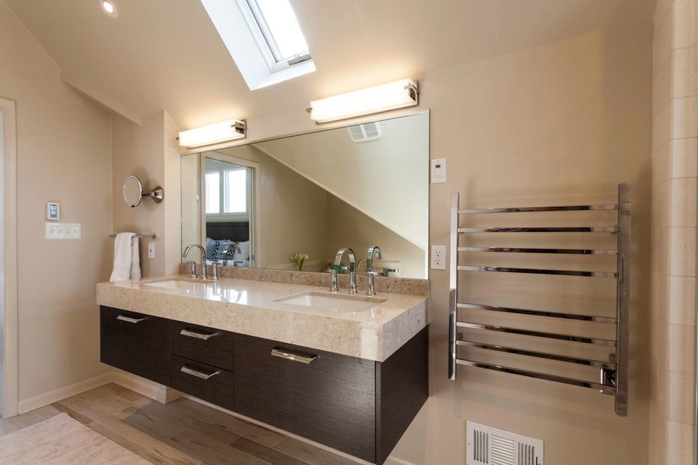 Photo of a modern master bathroom in Other with a drop-in sink, flat-panel cabinets, dark wood cabinets, a two-piece toilet, beige tile, pebble tile, beige walls and light hardwood floors.