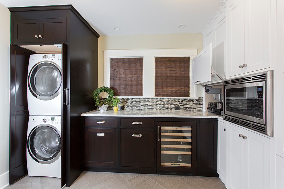 Mid-sized arts and crafts u-shaped laundry room in San Diego with raised-panel cabinets, dark wood cabinets, beige walls, travertine floors and a stacked washer and dryer.