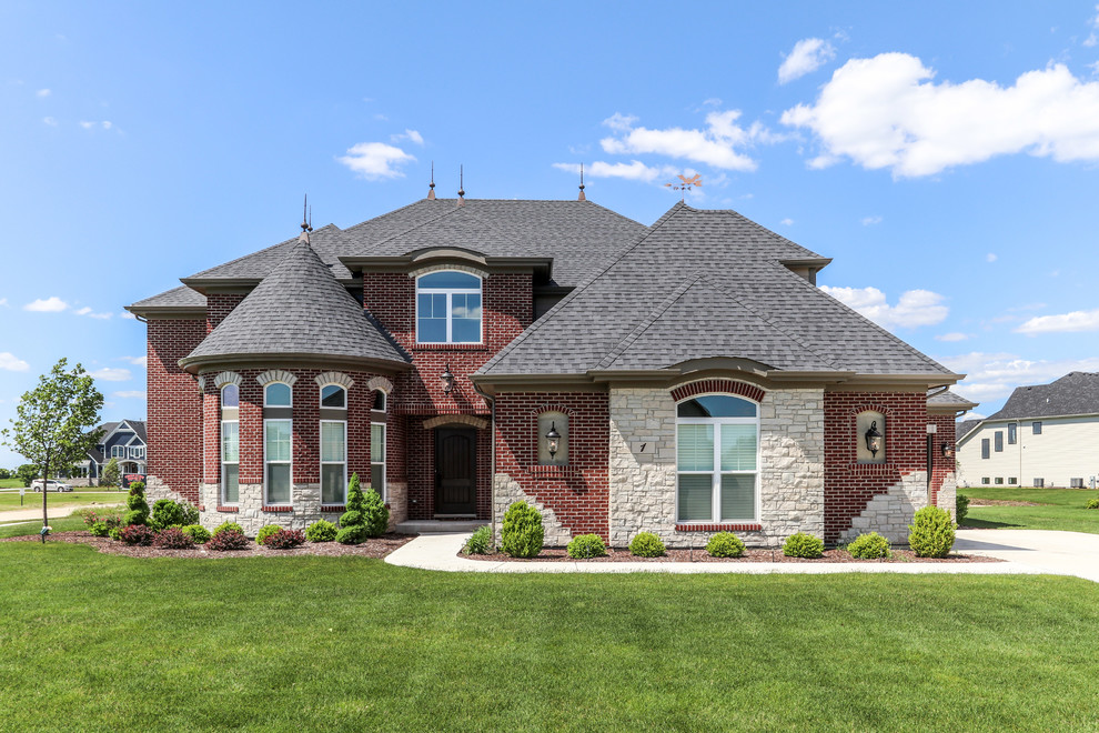 This is an example of a large traditional two-storey red house exterior in Chicago with stone veneer and a hip roof.