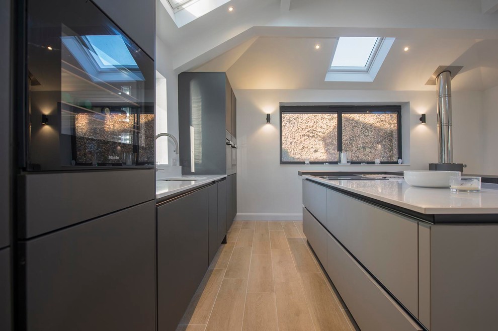Design ideas for a mid-sized contemporary galley eat-in kitchen in Other with an undermount sink, flat-panel cabinets, grey cabinets, quartzite benchtops, white splashback, stone slab splashback, black appliances, ceramic floors, with island, brown floor and white benchtop.