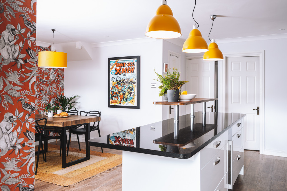This is an example of a mid-sized contemporary single-wall eat-in kitchen in Berkshire with an undermount sink, flat-panel cabinets, white cabinets, granite benchtops, orange splashback, cement tile splashback, coloured appliances, vinyl floors, with island, brown floor and black benchtop.