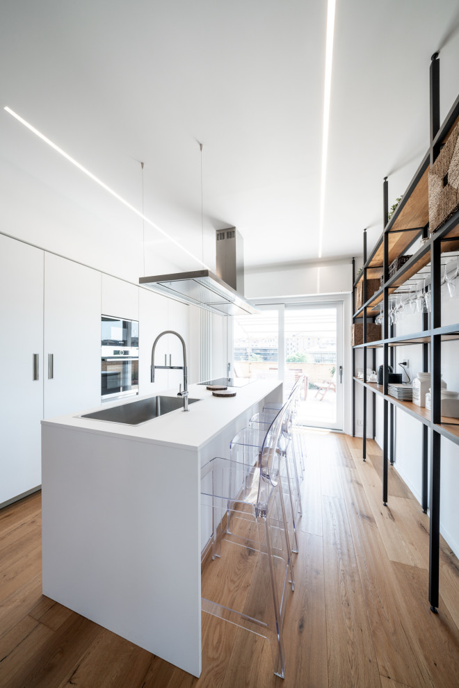 Design ideas for a contemporary galley kitchen in Rome with an undermount sink, flat-panel cabinets, white cabinets, medium hardwood floors, with island, brown floor and white benchtop.