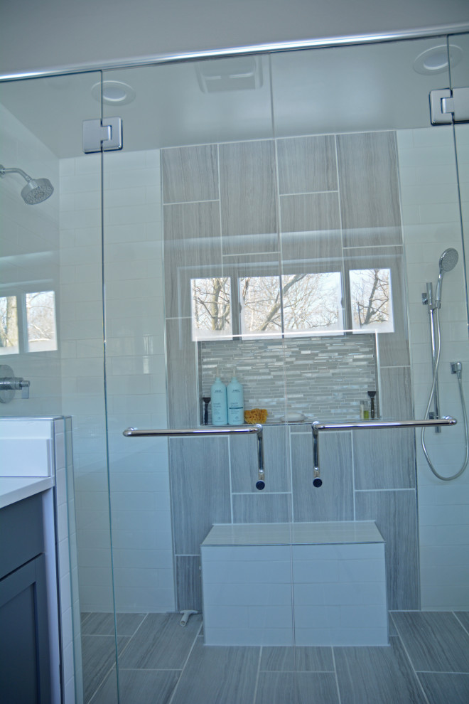 Inspiration for a large transitional master gray tile and porcelain tile porcelain tile, gray floor and double-sink walk-in shower remodel with shaker cabinets, gray cabinets, a two-piece toilet, white walls, an undermount sink, quartz countertops, a hinged shower door, white countertops, a niche and a built-in vanity