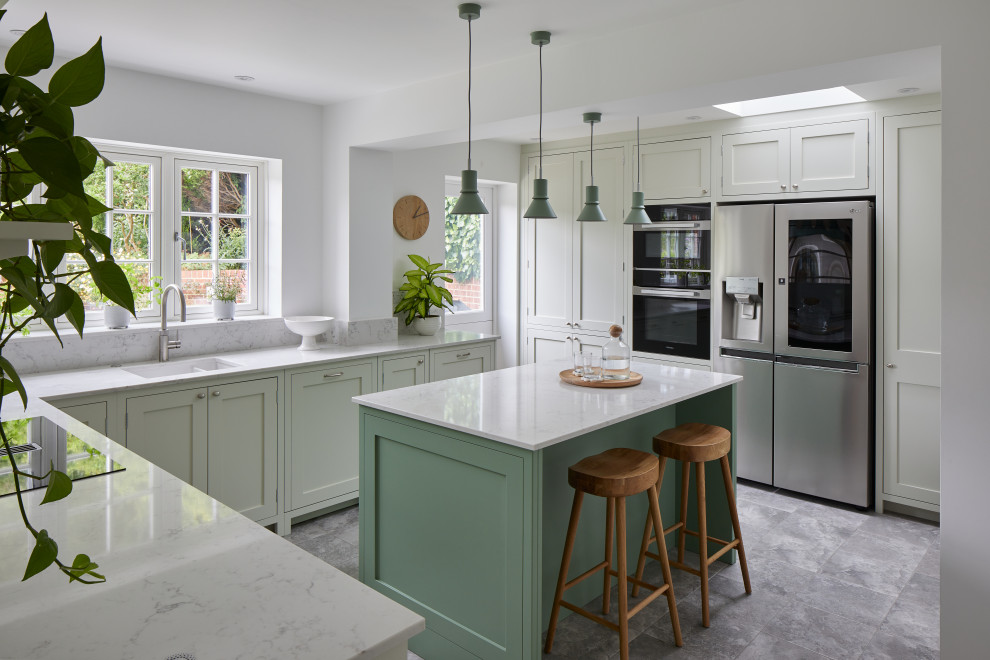 Inspiration for a mid-sized transitional l-shaped separate kitchen in London with a drop-in sink, shaker cabinets, green cabinets, quartzite benchtops, grey splashback, engineered quartz splashback, stainless steel appliances, ceramic floors, with island, grey floor and grey benchtop.