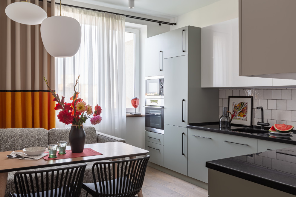 На фото: угловая кухня в стиле фьюжн с плоскими фасадами, белым фартуком, бежевым полом, черной столешницей и двухцветным гарнитуром