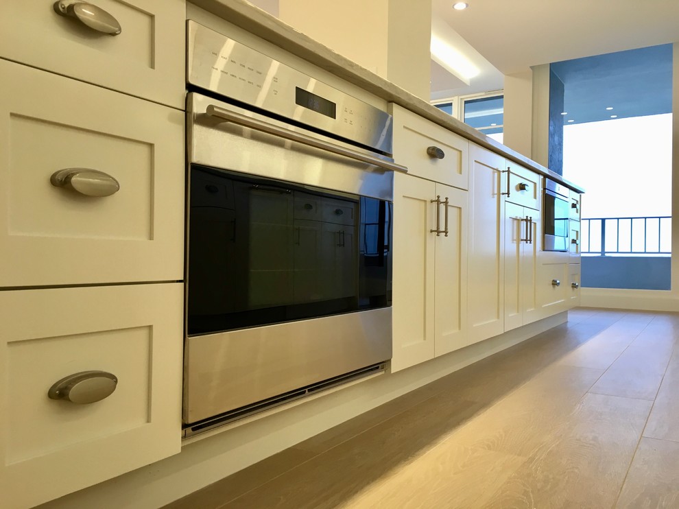 Example of a large transitional galley light wood floor and beige floor open concept kitchen design in Miami with an undermount sink, shaker cabinets, white cabinets, marble countertops, gray backsplash, marble backsplash, stainless steel appliances and an island