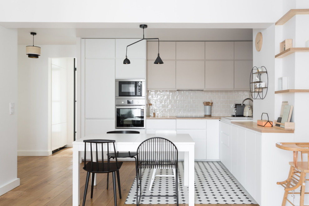 Photo of a large scandinavian l-shaped open plan kitchen in Paris with a single-bowl sink, beaded inset cabinets, white cabinets, wood benchtops, beige splashback, terra-cotta splashback, stainless steel appliances, porcelain floors, no island, multi-coloured floor and beige benchtop.