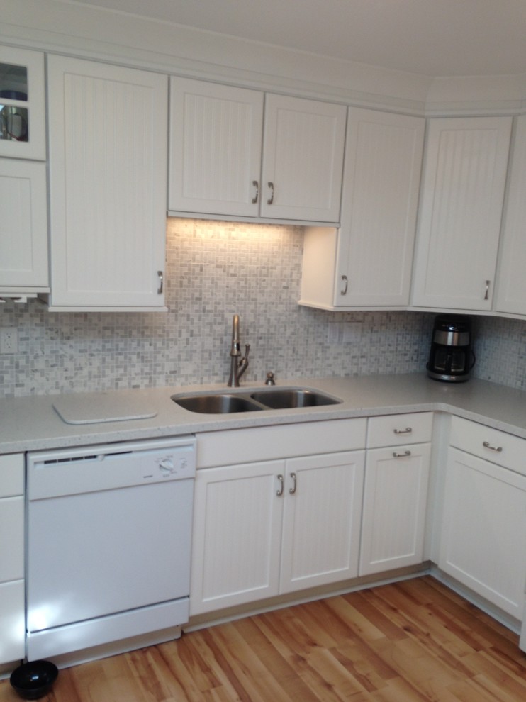 Eat-in kitchen - mid-sized coastal l-shaped eat-in kitchen idea with an undermount sink, beaded inset cabinets, white cabinets, solid surface countertops, gray backsplash, mosaic tile backsplash, white appliances and a peninsula