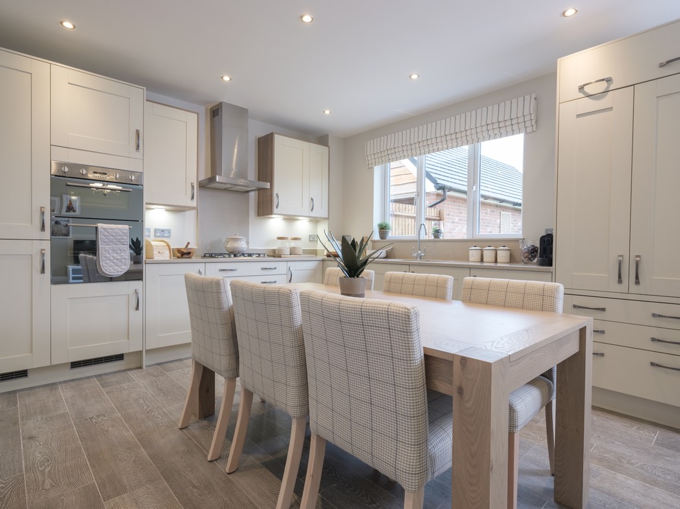 Inspiration for a large modern l-shaped eat-in kitchen in Essex with a drop-in sink, recessed-panel cabinets, white cabinets, quartz benchtops, white splashback, metal splashback, stainless steel appliances, porcelain floors, no island, brown floor and beige benchtop.