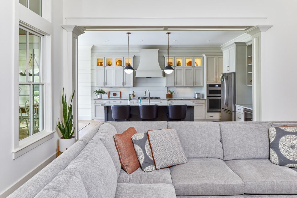 Inspiration for a large transitional l-shaped light wood floor and brown floor open concept kitchen remodel with a farmhouse sink, flat-panel cabinets, gray cabinets, granite countertops, white backsplash, wood backsplash, stainless steel appliances, an island and white countertops