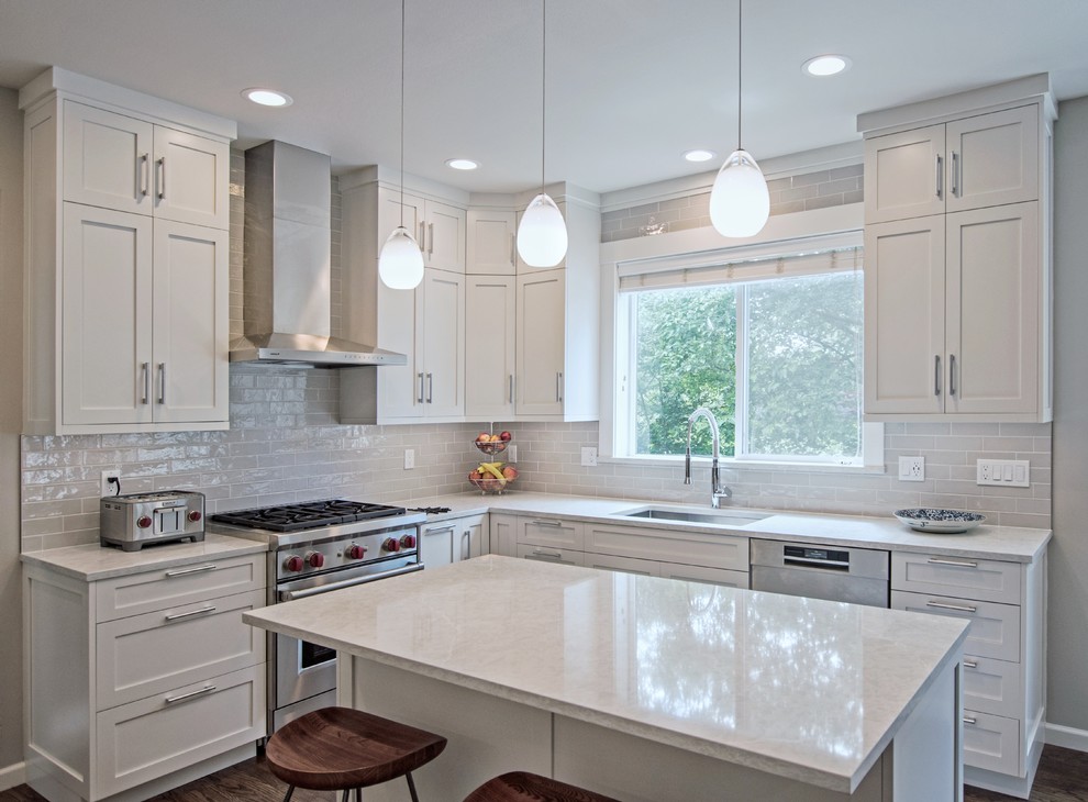 Example of a mid-sized transitional l-shaped dark wood floor and brown floor eat-in kitchen design in Seattle with a drop-in sink, shaker cabinets, white cabinets, quartz countertops, white backsplash, ceramic backsplash, stainless steel appliances, an island and white countertops