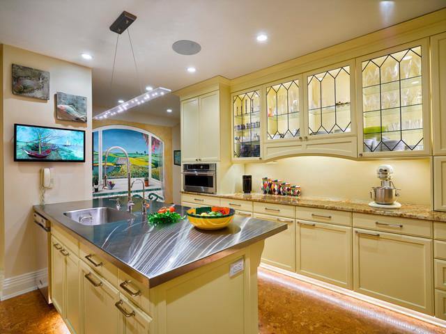 Mid-sized transitional u-shaped kitchen pantry in Cleveland with an integrated sink, glass-front cabinets, yellow cabinets, stainless steel benchtops, yellow splashback, glass sheet splashback, stainless steel appliances, cork floors, with island, brown floor and multi-coloured benchtop.