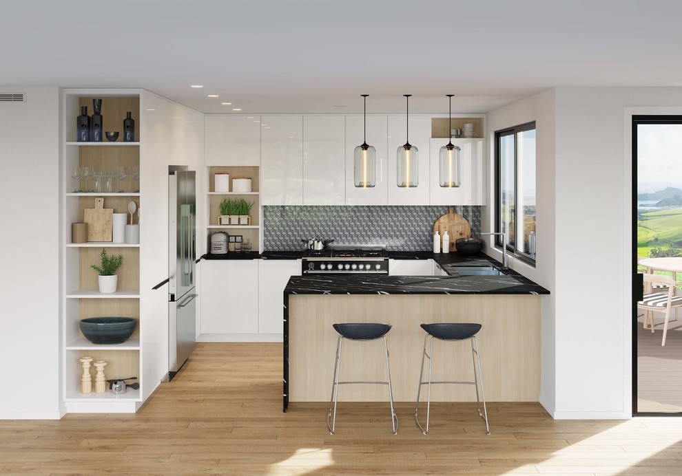 Contemporary u-shaped kitchen in Auckland with a double-bowl sink, flat-panel cabinets, white cabinets, quartz benchtops, multi-coloured splashback, glass sheet splashback, black appliances, with island and black benchtop.