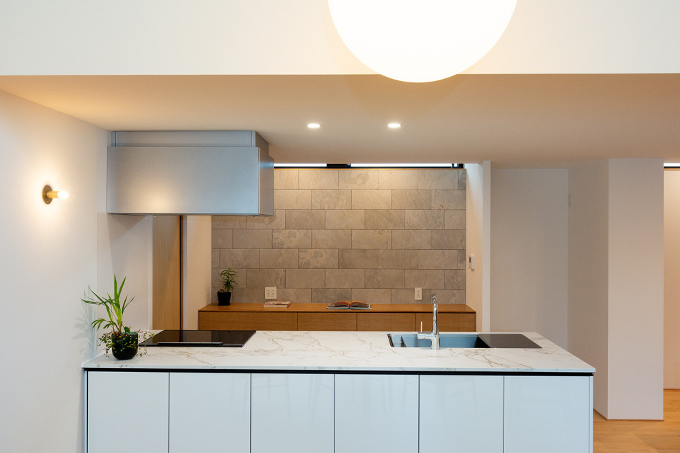Photo of an expansive single-wall open plan kitchen in Other with an undermount sink, flat-panel cabinets, white cabinets, quartz benchtops, white splashback, shiplap splashback, black appliances, light hardwood floors, with island, white benchtop and wallpaper.