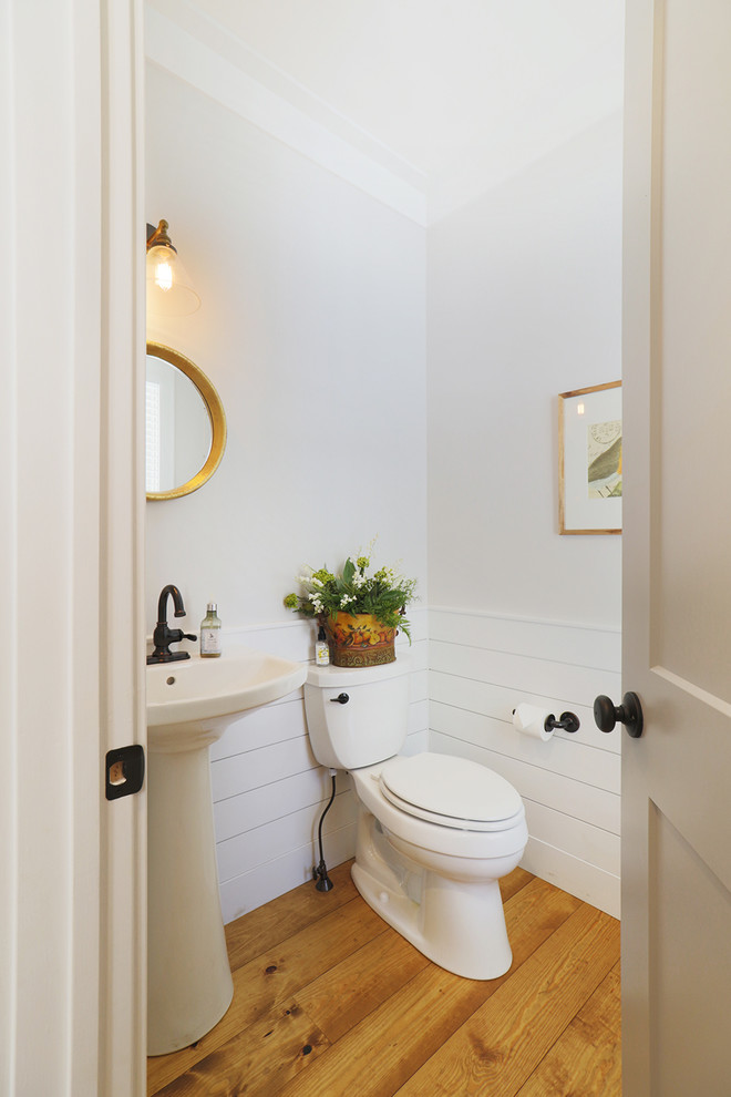 Inspiration for a small traditional powder room in Other with a two-piece toilet, white walls, light hardwood floors, a pedestal sink and beige floor.