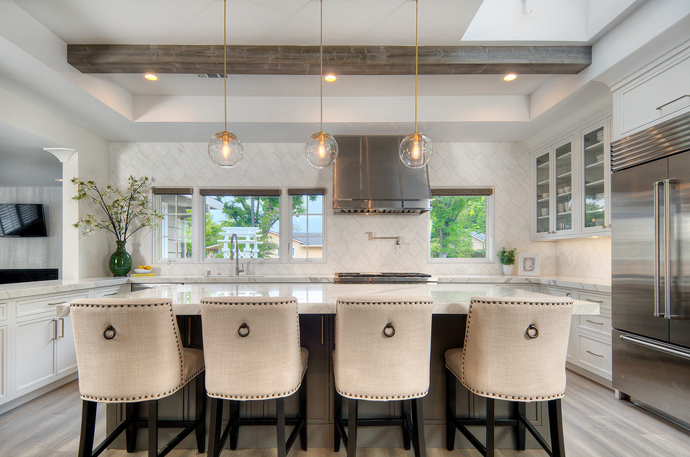 This is an example of a large traditional u-shaped kitchen in San Francisco with glass-front cabinets, white cabinets, white splashback, stainless steel appliances, with island, beige floor, white benchtop, marble benchtops and marble splashback.